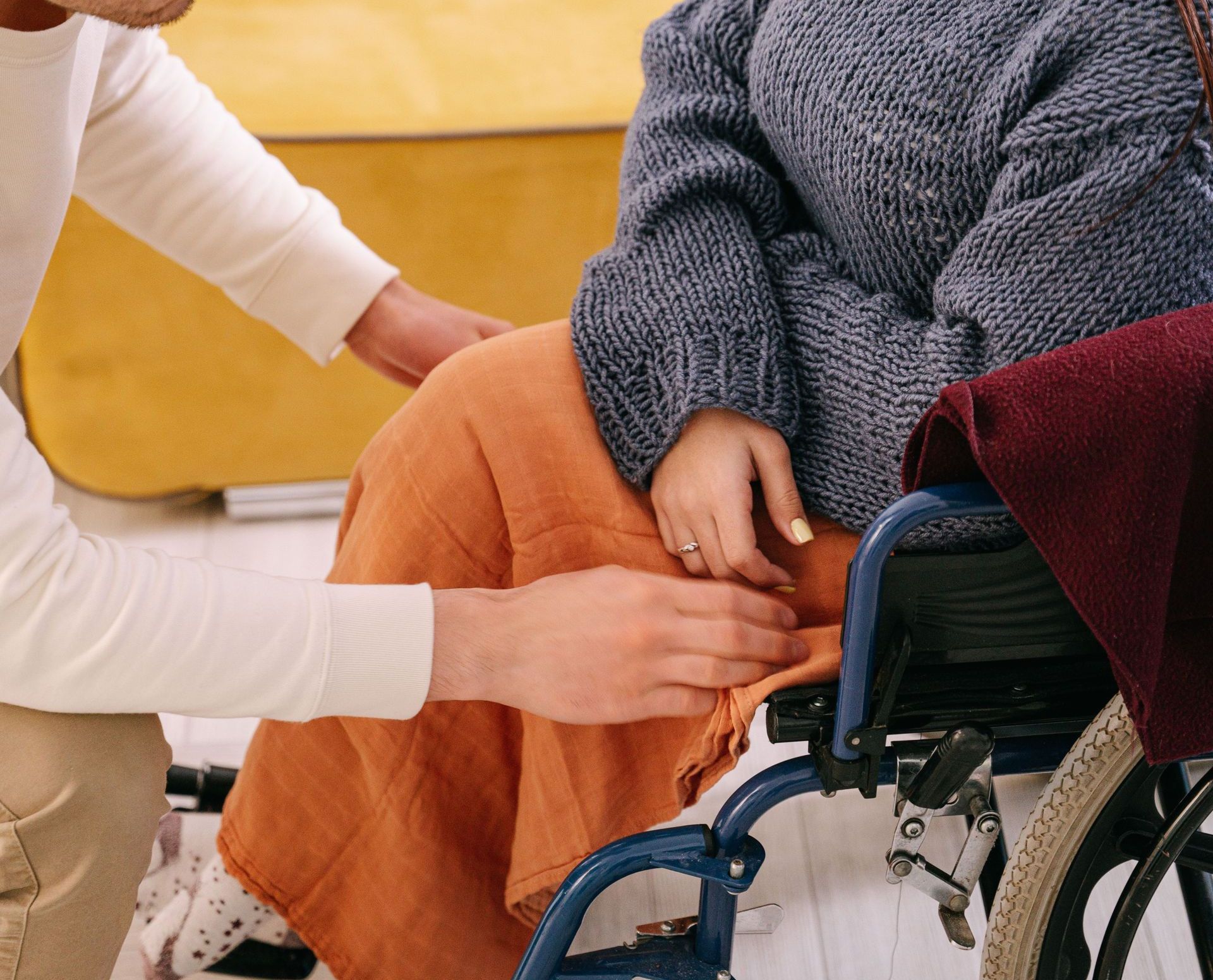 A supportive man assisting a woman in a wheelchair indoors, reflecting care and companionship.