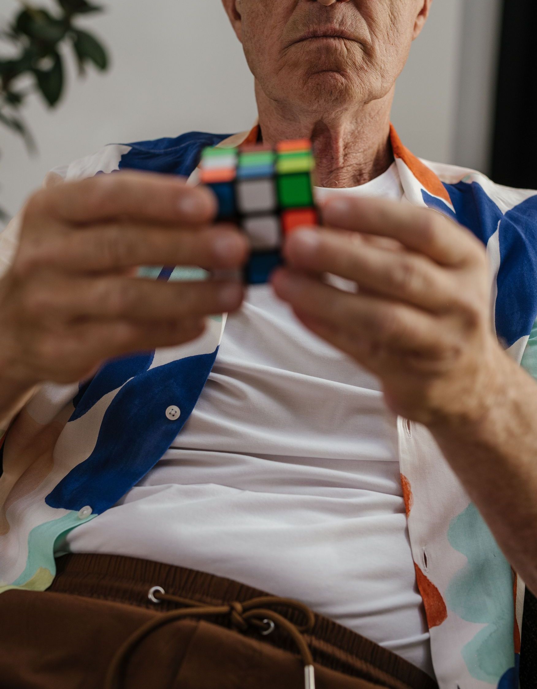 Elderly man focusing on solving a Rubik's Cube indoors, demonstrating concentration and puzzle-solving skills.